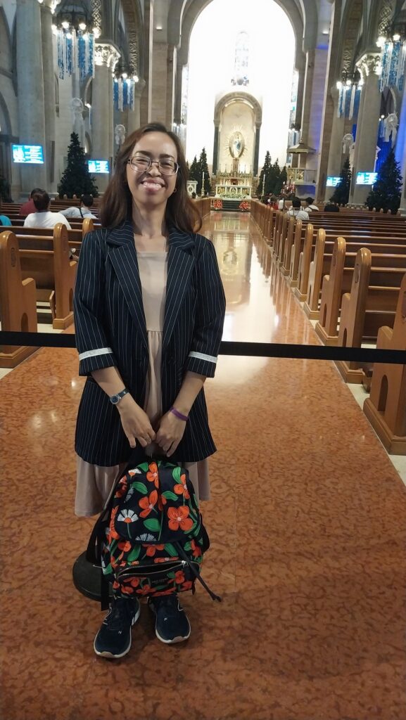 woman in front of the church hallway, with altar at the background.